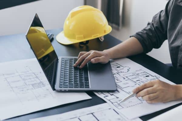 Engineer reviewing construction blueprints and data on laptop, representing expert witness analysis for legal cases
