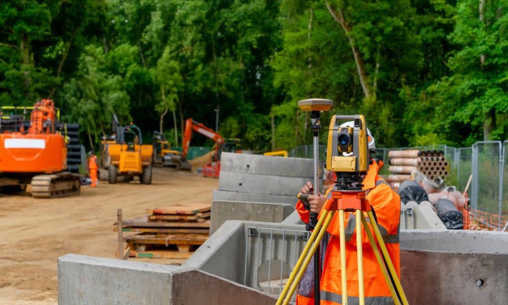 Construction surveyor measuring land with a total station at an active construction site