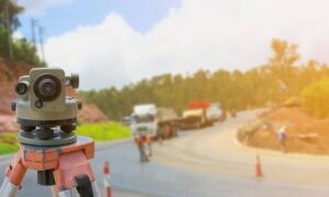 Construction survey equipment on a tripod at a highway project site with workers and traffic in the background