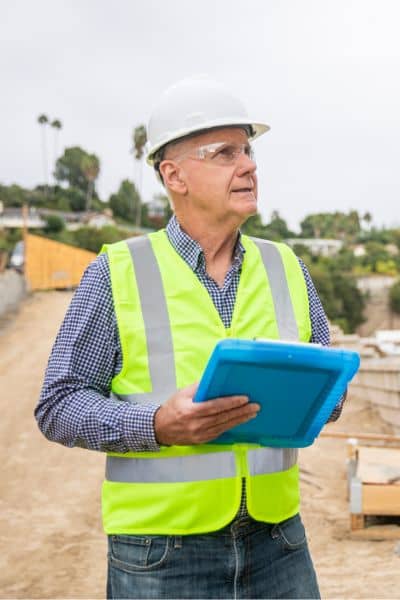 Engineer conducting dam inspection field assessment - ALTA SURVEY Texas Civil engineer inspecting an earthen dam structure with a clipboard during a field assessment