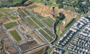 Aerial view of a housing subdivision with land divided into lots, roads, and nearby homes during early development