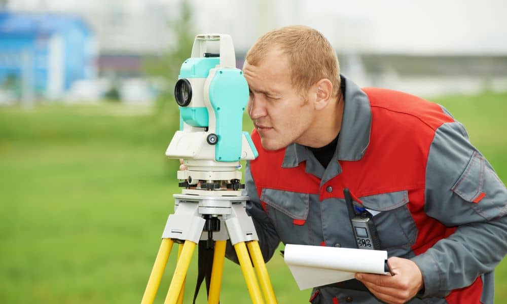Surveyor measuring a property line with equipment during a boundary survey to determine boundary survey price