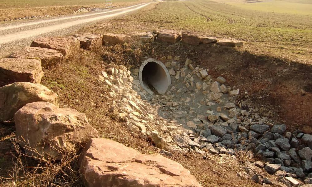 A culvert pipe under a rural driveway with surrounding rocks and drainage, illustrating proper drainage design on the property