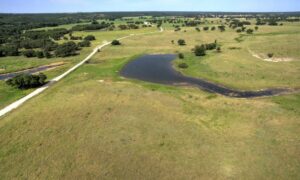 Aerial view of a rural ranch with a stock tank, open grassland, and surrounding terrain, showing the type of landscape LiDAR mapping can help document